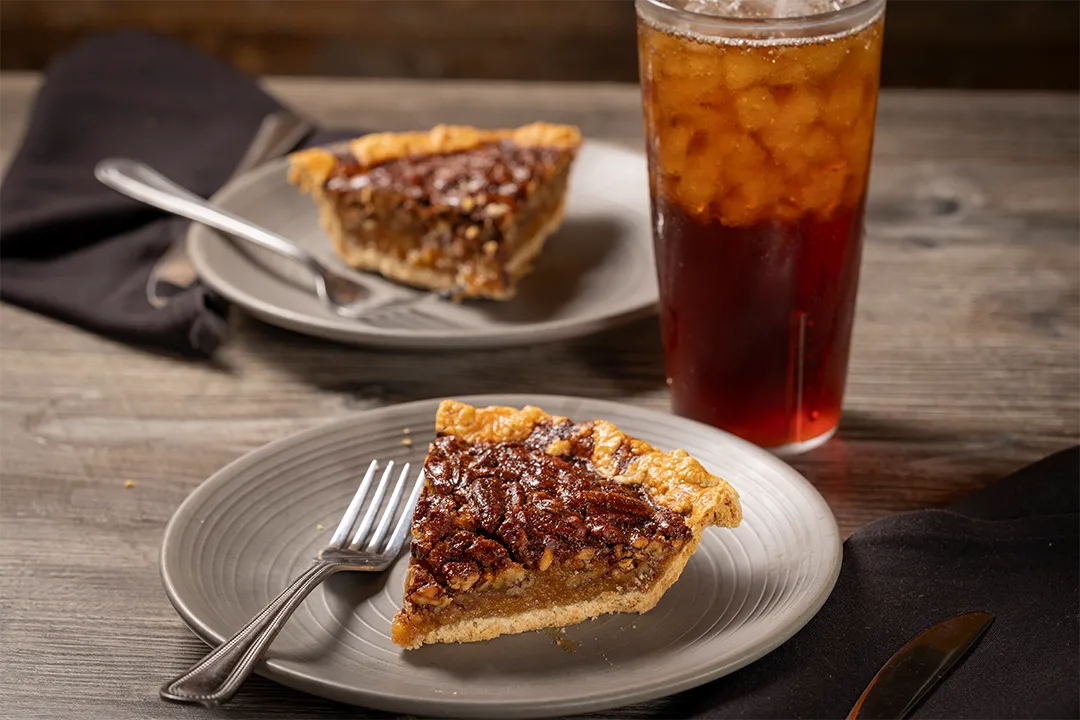 Two slices of pecan pie and a glass of tea.